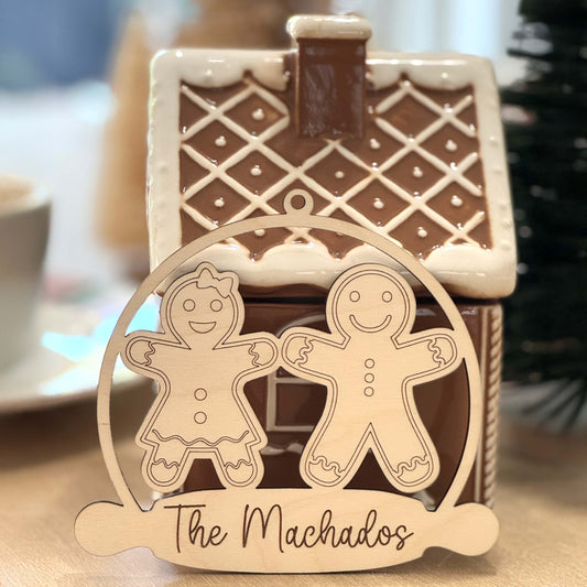 Personalized wooden gingerbread family ornament engraved with the family name in front of a gingerbread house.