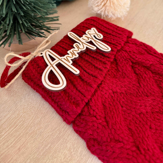 Red cable-knit Christmas stocking featuring a personalized wooden name tag reading “Annelys,” attached with jute twine.
