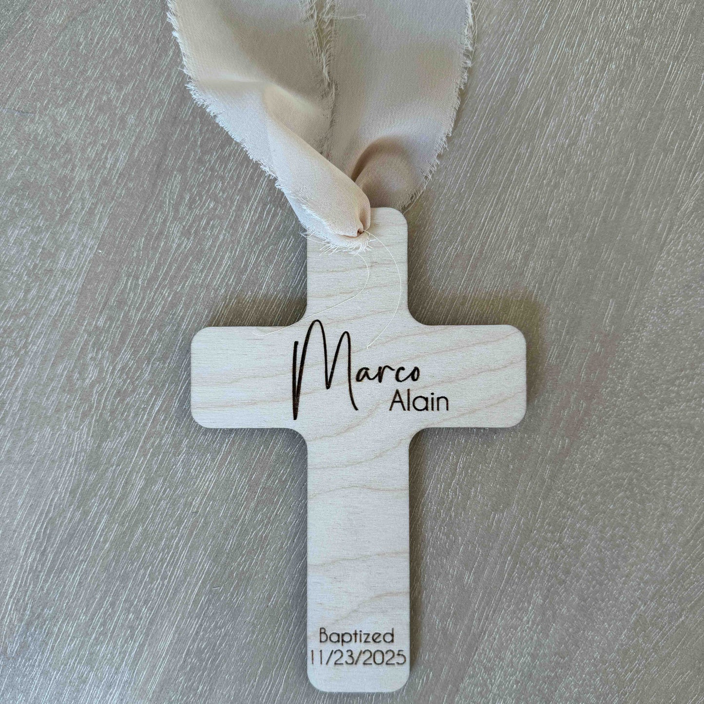 Personalized baptism favor cross with beige chiffon ribbon on wood background