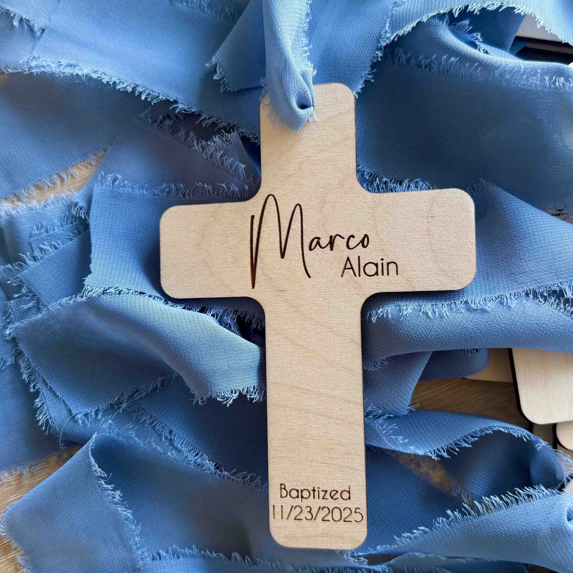 Engraved birch wood baptism favor cross with blue ribbon, close-up view