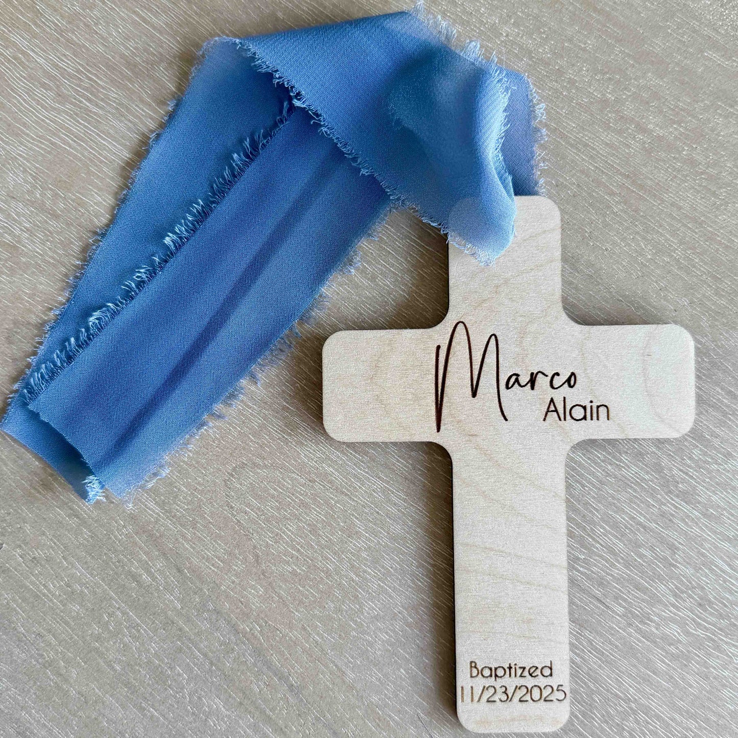 Personalized baptism favor cross with dusty blue chiffon ribbon on wood background