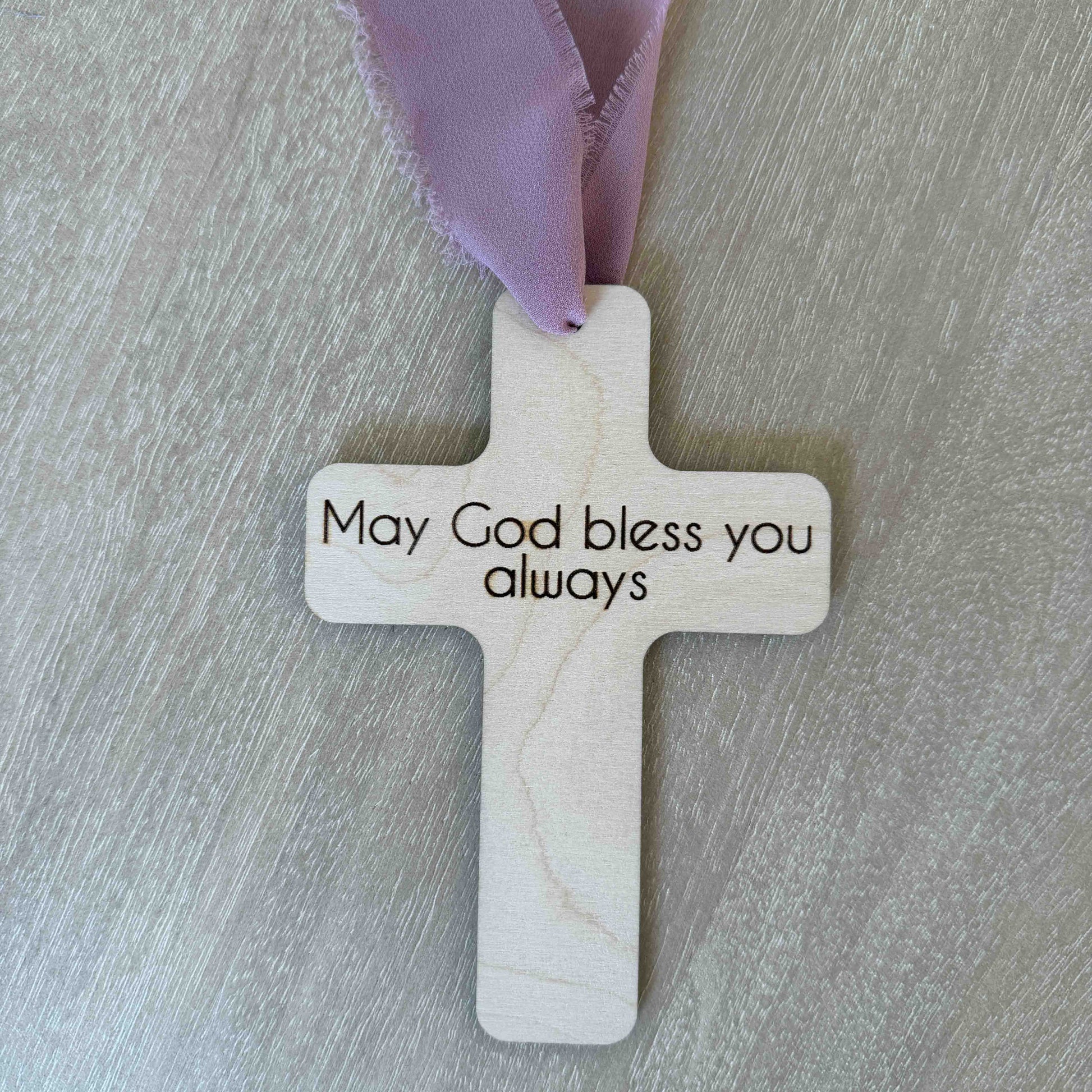 Personalized baptism favor cross with message on back mauve chiffon ribbon on wood background