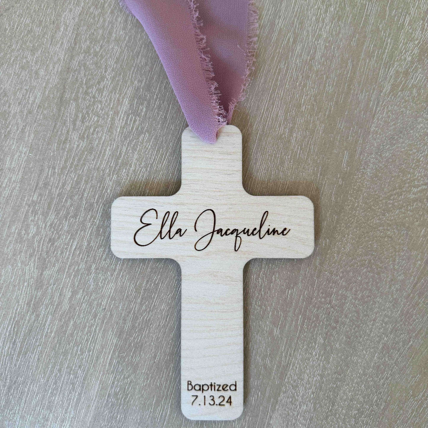Personalized baptism favor cross with mauve chiffon ribbon on wood background