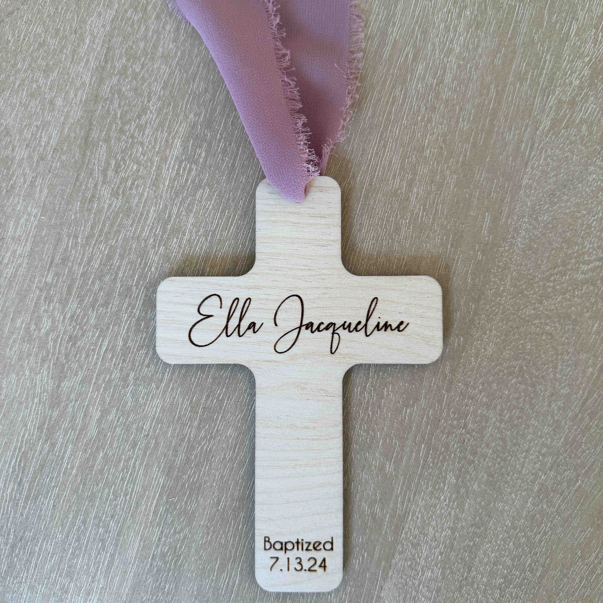 Personalized baptism favor cross with mauve chiffon ribbon on wood background
