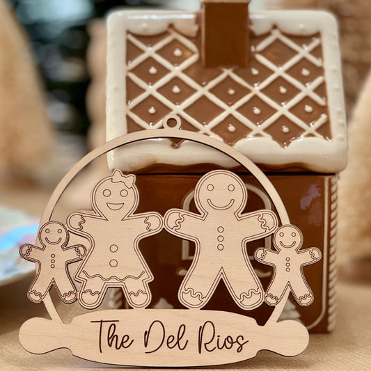 Personalized wooden gingerbread family ornament engraved with the family name in front of a gingerbread house.
