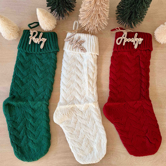Set of three knit Christmas stockings in green, white, and red, each accented with a personalized wooden script name tag.