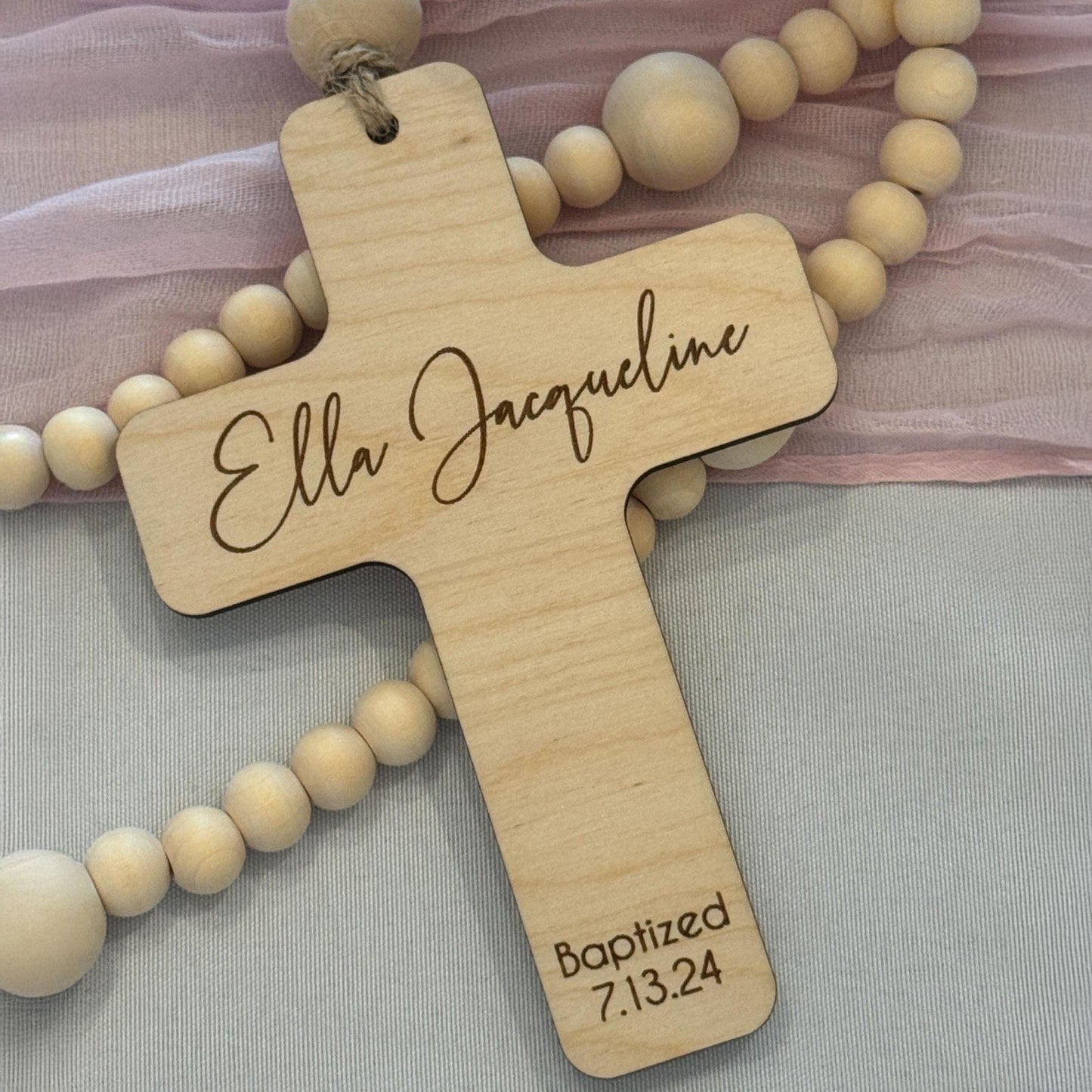 Personalized wooden rosary with engraved birch cross showing the name Ella Jacqueline and baptism date.
